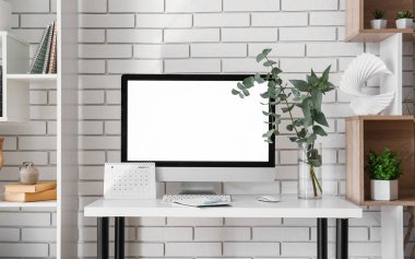 Bilgisayarlı işyeri, vazoya dallar yerleştirmek ve beyaz tuğla duvarın yanındaki rafları yerleştirmek.