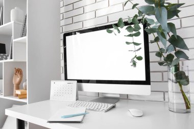 Bilgisayarlı işyeri, vazoya şubeler ve beyaz tuğla duvarın yanına takvim