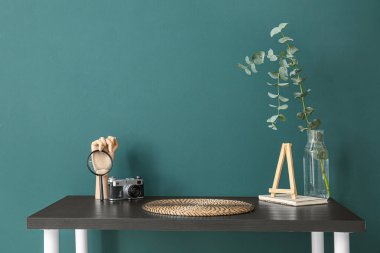 Vazoda okaliptüs bulunan işyeri, ahşap el, fotoğraf makinesi ve yeşil duvarın yanında büyüteç.