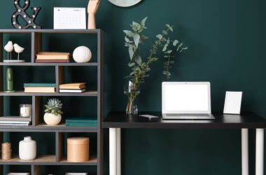 Laptoplu işyeri, vazoya dallar ve yeşil duvarın yanındaki çerçeve.