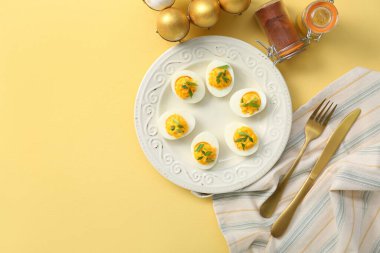 Sarı arka planda içi doldurulmuş yumurta, çatal bıçak, peçete ve baharatla dolu bir tabak. Paskalya kutlaması