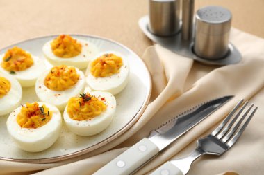 Lezzetli doldurulmuş yumurta, bej arka planda peçete ve çatal bıçak takımı, yakın plan. Paskalya kutlaması