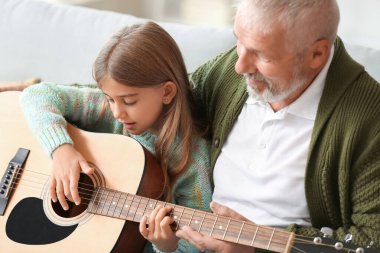 Büyük adam küçük torununa evde gitar çalmayı öğretiyor.