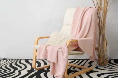 Kol sandalyesi, pembe ekose ve vazo, ışık duvarı yanında.