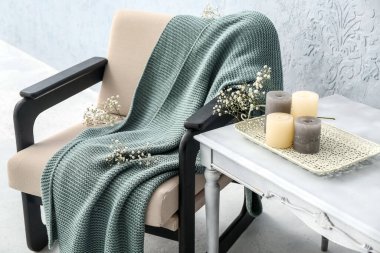 Ekoseli koltuk, çiçekler, masa ve ışık duvarının yanındaki mumlar.