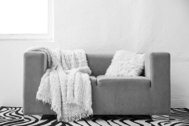 Beyaz battaniyeli gri kanepe ve ışık duvarının yanında yastık.