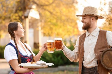 Adam ve garson, Ekim Festivali 'ni dışarıda kutlarken bardakları birayla tokuşturuyorlar.