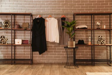 Gri tuğla duvarın yanında aksesuarlı ve elbiseli raf üniteleri