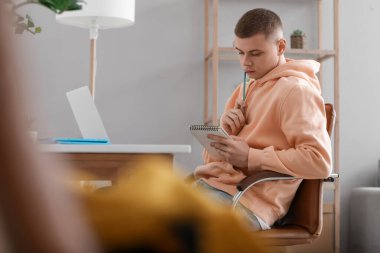 Genç adam evde çalışırken notlar yazıyor.