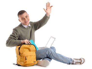 Dizüstü bilgisayarı olan erkek öğrenci beyaz arka planda sırt çantasından not defteri alıyor.