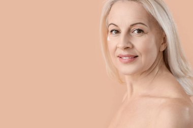 Bej arka planda sağlıklı cilde sahip olgun sarışın kadın, yakın plan.