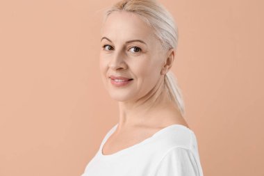 Bej arka planda sağlıklı ciltli olgun sarışın kadın.