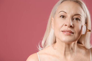 Pembe arka planda yüz masajı aleti olan olgun sarışın kadın, yakın plan.