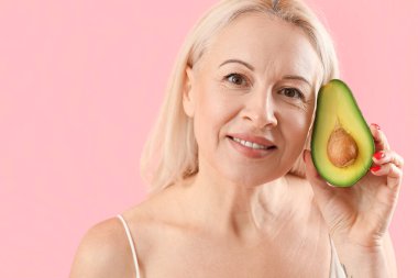 Pembe arka planda avokadosu olan olgun sarışın kadın, yakın plan.