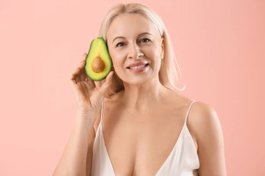 Pembe arka planda avokadosu olan olgun sarışın kadın.