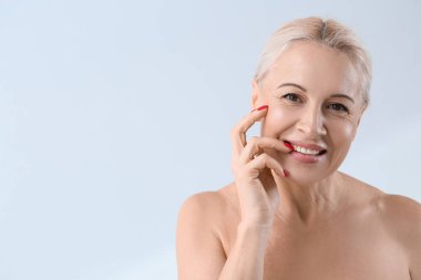 Açık arkaplanda gülümseyen sağlıklı ciltli olgun sarışın kadın, yakın plan.