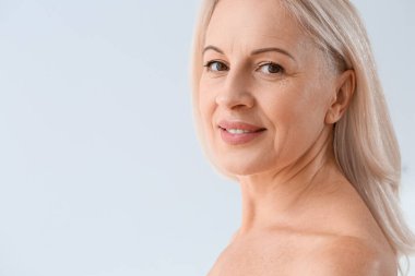 Açık arkaplanda gülümseyen sağlıklı ciltli olgun sarışın kadın, yakın plan.