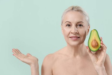 Avokadosu olan olgun sarışın kadın yeşil arka planda bir şey gösteriyor.