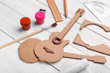 Beyaz ahşap arka planda materyalleri olan karton gitar oyuncağı.