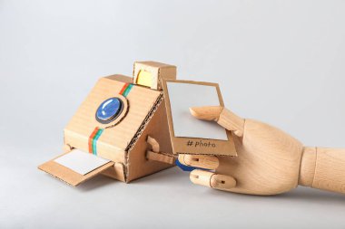 Karton fotoğraf makinesi ve arka planda resim olan tahta el.