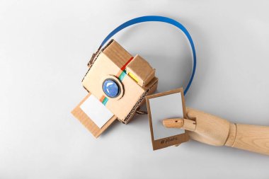 Karton fotoğraf makinesi ve arka planda resim olan tahta el.