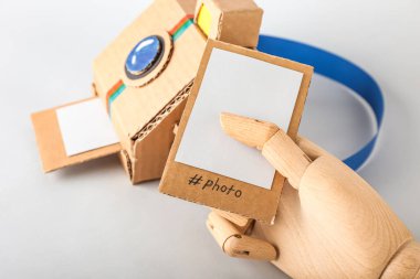 Karton fotoğraf makinesi ve arka planda resim olan ahşap el, yakın plan.