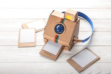 Beyaz ahşap zemin üzerinde resimler olan karton fotoğraf makinesi.