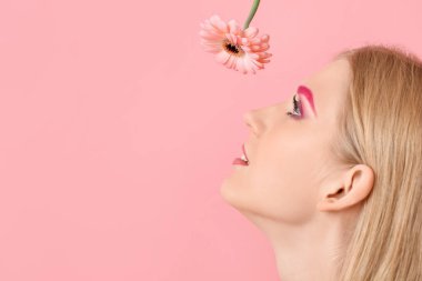 Yaratıcı kaşları olan genç bir kadın Gerbera çiçeğine bakıyor.