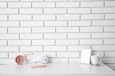 Alarm saati, kalem kutusu, çerçevesi ve bardağı beyaz tuğla duvarın yanında olan işyeri