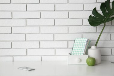 Cep telefonlu işyeri, vazoda palmiye yaprağı, defterler ve beyaz tuğla duvarın yanında elma.