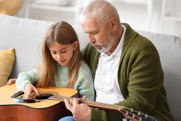Büyük adam küçük torununa evde gitar çalmayı öğretiyor.