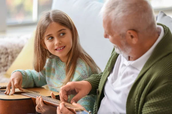 Büyük adam küçük torununa evde gitar çalmayı öğretiyor.
