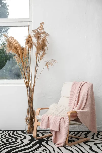 Kol sandalyesi, pembe ekose ve vazo, ışık duvarı yanında.