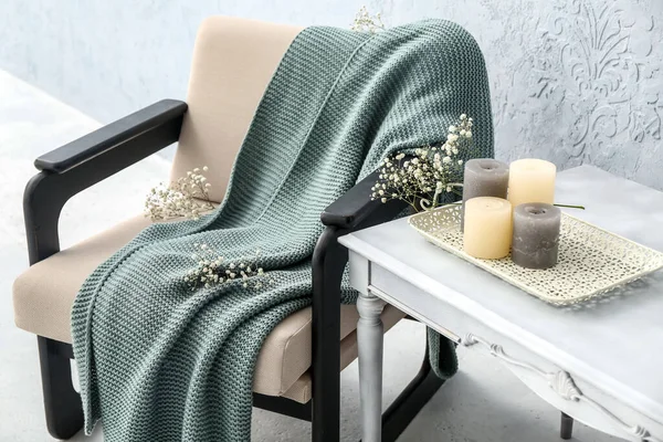 Ekoseli koltuk, çiçekler, masa ve ışık duvarının yanındaki mumlar.