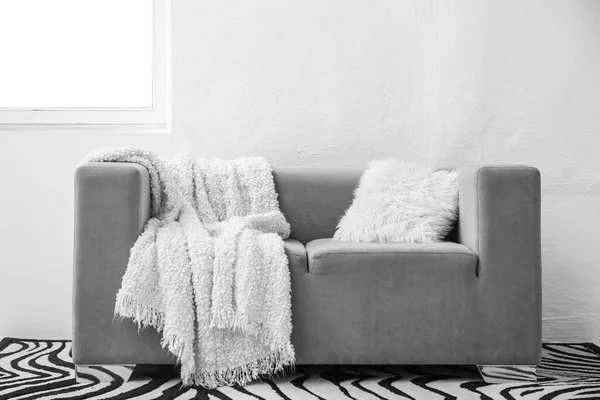 Beyaz battaniyeli gri kanepe ve ışık duvarının yanında yastık.