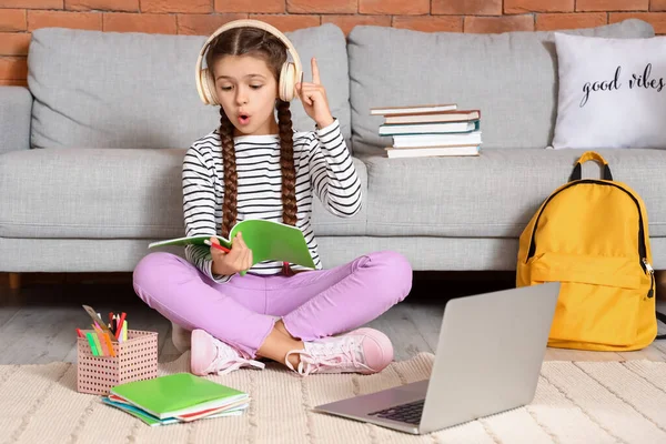 Little girl in headphones having idea while studying with online tutor at home