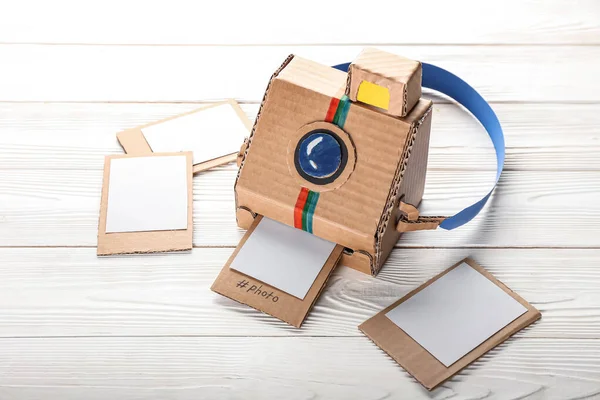 Beyaz ahşap zemin üzerinde resimler olan karton fotoğraf makinesi.