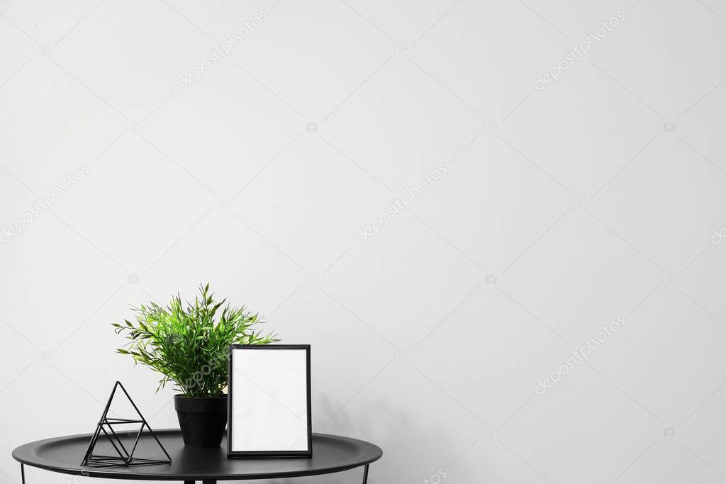 Table with frame, houseplant and decor near light wall