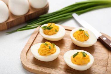 Beyaz arka planda içi doldurulmuş yumurta ve bıçak dolu bir tahta, yakın plan. Paskalya kutlaması