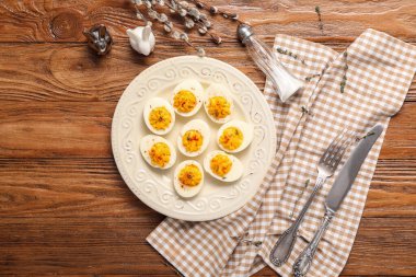 Doldurulmuş yumurta, çatal bıçak, peçete, söğüt dalları ve ahşap arka planda Paskalya tavşanları.