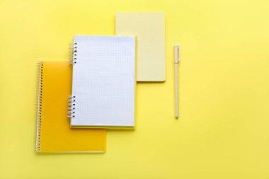 Sarı arkaplandaki defterler ve kalemler