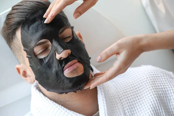 Cosmetologue Appliquer Masque Feuille Sur Visage Jeune Homme Dans Salon — Photo