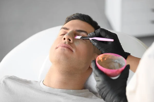 Kosmetolog Nakładający Glinianą Maskę Twarz Młodego Mężczyzny Salonie Zbliżenie — Zdjęcie stockowe