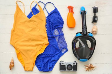 Dalış maskeli kadın plaj aksesuarları ve beyaz ahşap arka planda fotoğraf makinesi.