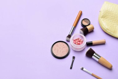 Mor arka planda makyaj fırçaları ve kozmetik ürünleri