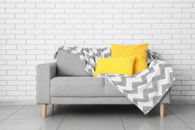 Yastıklı ve ekoseli modern kanepe odada tuğla duvarın yanında.