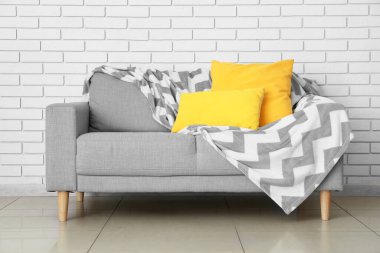 Yastıklı ve ekoseli modern kanepe odada tuğla duvarın yanında.