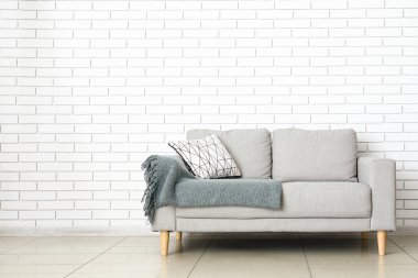 Yastıklı ve ekoseli modern kanepe odada tuğla duvarın yanında.
