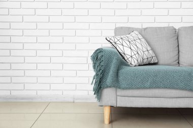 Yastıklı ve ekoseli modern kanepe odada tuğla duvarın yanında.
