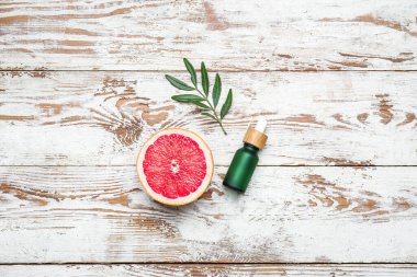 Hafif ahşap zemin üzerinde greyfurt ve gerekli yağ şişesinin yarısıyla kompozisyon